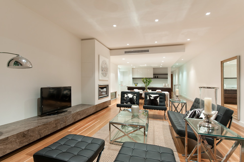 Photo of a mid-sized contemporary open concept family room in Adelaide with white walls, medium hardwood floors, a standard fireplace, a plaster fireplace surround and a freestanding tv.