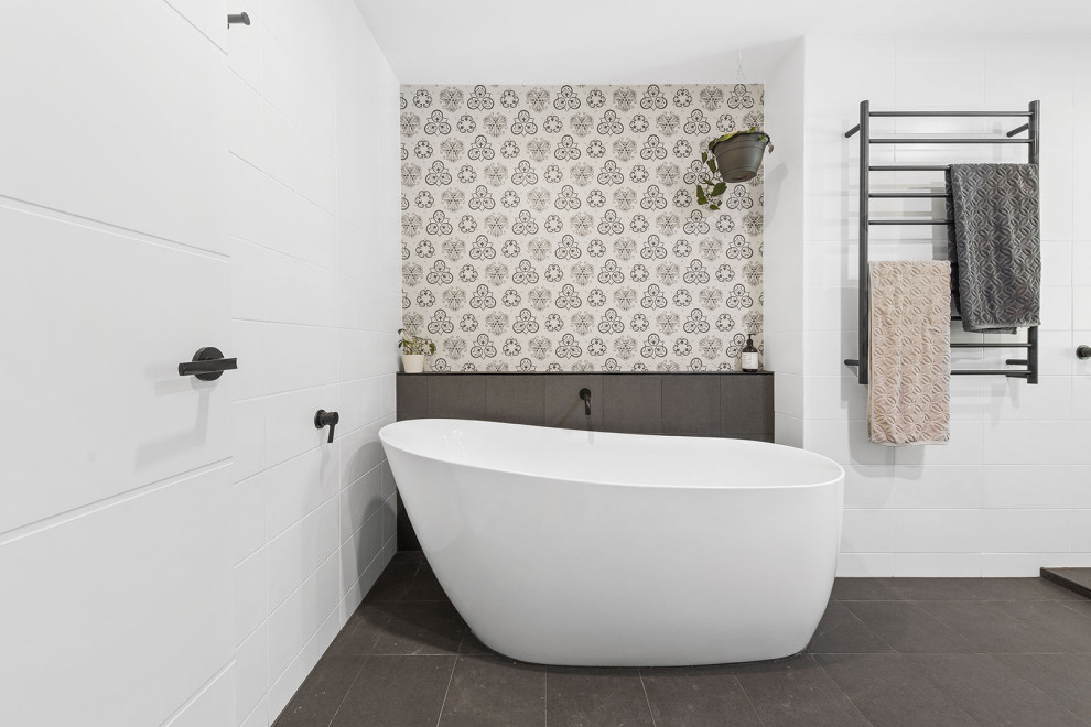 Photo of a mid-sized beach style master bathroom in Sunshine Coast with a freestanding tub, white tile, white walls and black floor.