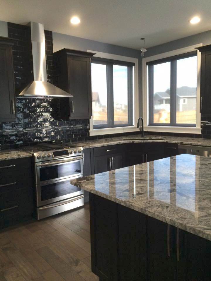 Contemporary u-shaped open plan kitchen in Calgary with an undermount sink, shaker cabinets, dark wood cabinets, granite benchtops, blue splashback, glass tile splashback, stainless steel appliances, dark hardwood floors and with island.