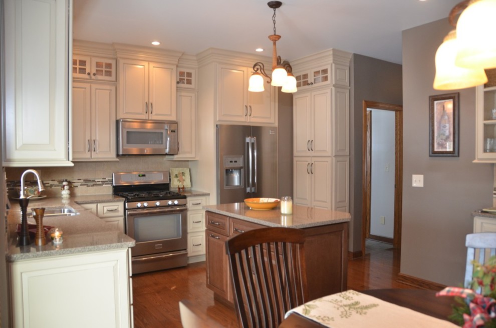 Example of a mid-sized transitional medium tone wood floor and brown floor eat-in kitchen design with stainless steel appliances, an island, a double-bowl sink, raised-panel cabinets, white cabinets, granite countertops, multicolored backsplash and matchstick tile backsplash