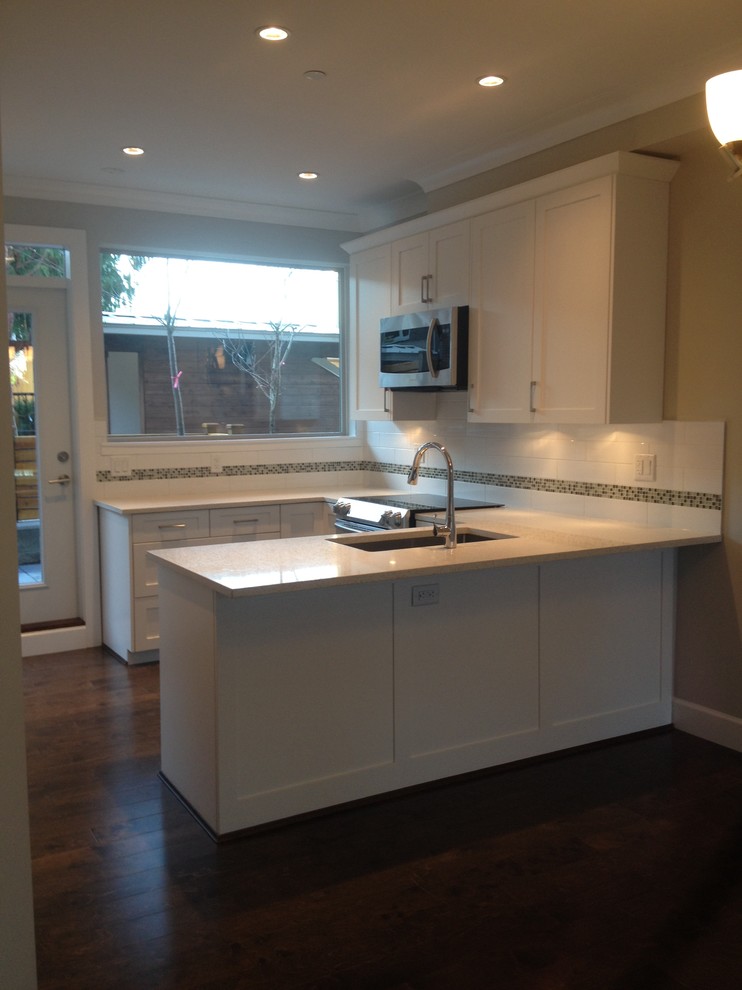 Photo of a small traditional u-shaped eat-in kitchen in Vancouver with an undermount sink, flat-panel cabinets, white cabinets, quartzite benchtops, white splashback, ceramic splashback, stainless steel appliances, dark hardwood floors and a peninsula.