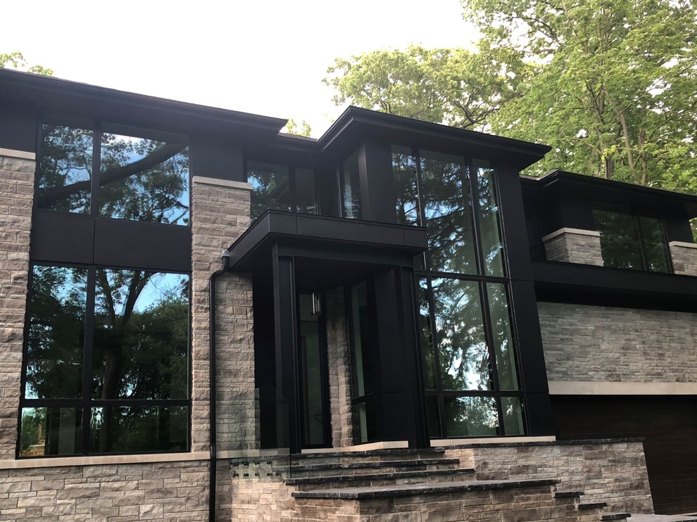 Inspiration for a large contemporary two-storey black house exterior in Toronto with a hip roof, a shingle roof, stone veneer and a black roof.