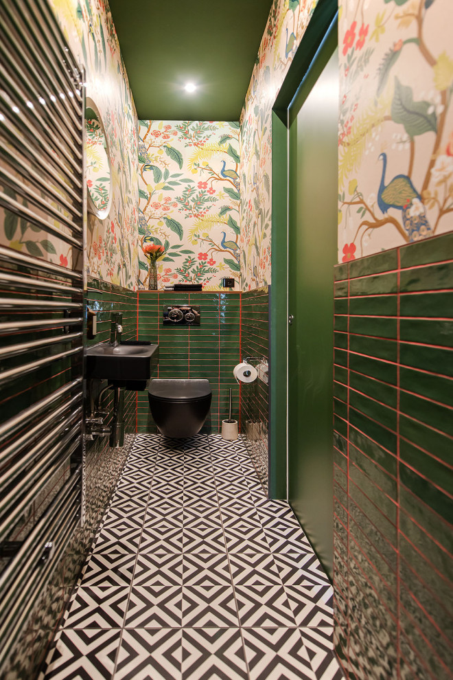 This is an example of a small eclectic master bathroom in Berlin with an alcove shower, a two-piece toilet, green tile, ceramic tile, beige walls, cement tiles, a wall-mount sink, black floor, a hinged shower door, a single vanity and wallpaper.