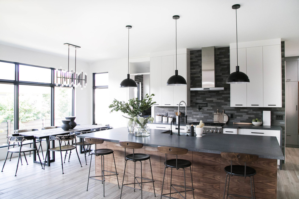 Contemporary galley eat-in kitchen in Salt Lake City with a farmhouse sink, flat-panel cabinets, white cabinets, black splashback, stainless steel appliances, with island, brown floor and black benchtop.