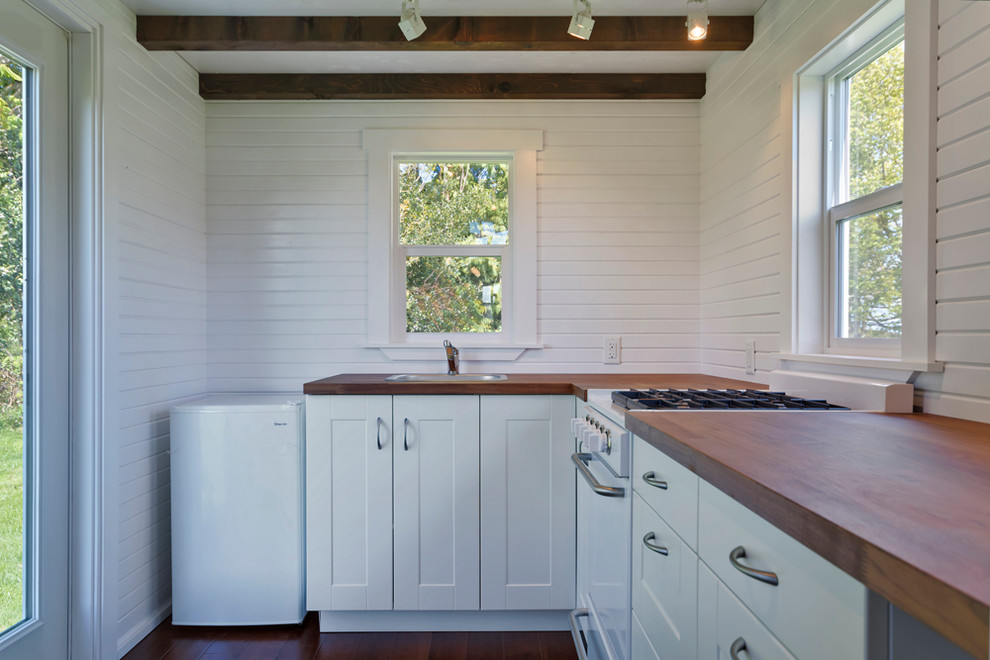 Inspiration for a small traditional l-shaped open plan kitchen in Vancouver with a drop-in sink, flat-panel cabinets, white cabinets, wood benchtops, white appliances and dark hardwood floors.