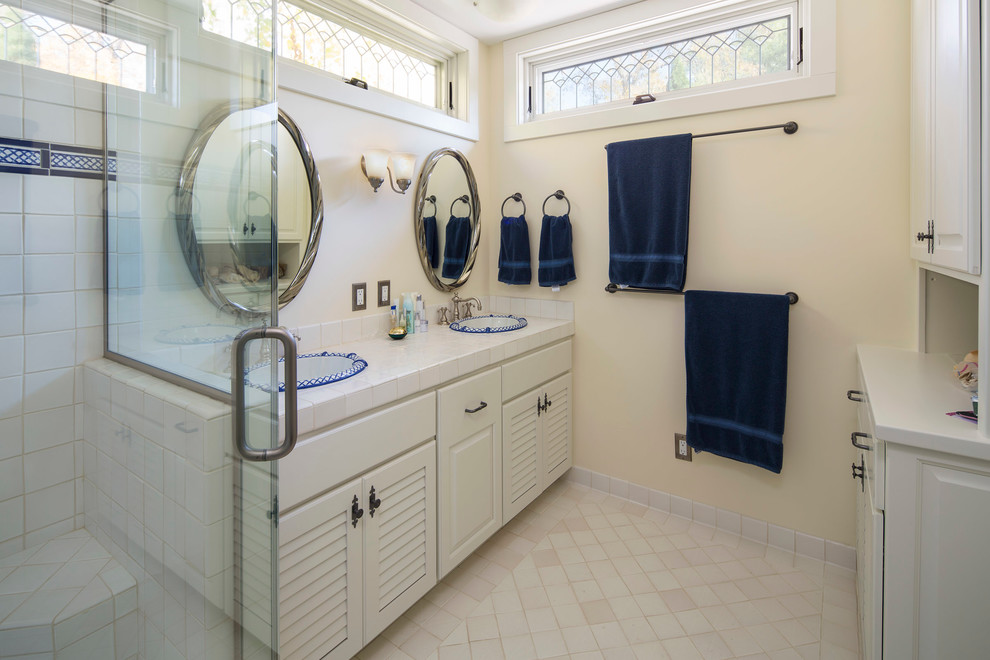 Inspiration for a traditional bathroom in Minneapolis with louvered cabinets, white cabinets, an alcove shower, white tile, ceramic tile, yellow walls, ceramic floors, a drop-in sink, tile benchtops, beige floor and a hinged shower door.