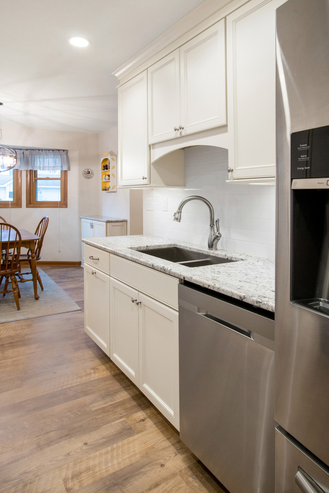 Mid-sized contemporary galley eat-in kitchen in Milwaukee with an undermount sink, recessed-panel cabinets, white cabinets, granite benchtops, white splashback, ceramic splashback, stainless steel appliances, vinyl floors, beige floor and multi-coloured benchtop.