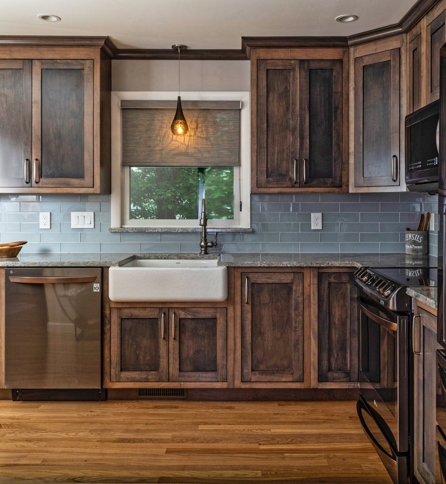 Photo of a mid-sized country u-shaped eat-in kitchen in Providence with a farmhouse sink, recessed-panel cabinets, dark wood cabinets, granite benchtops, blue splashback, subway tile splashback, stainless steel appliances, medium hardwood floors, no island, brown floor and multi-coloured benchtop.