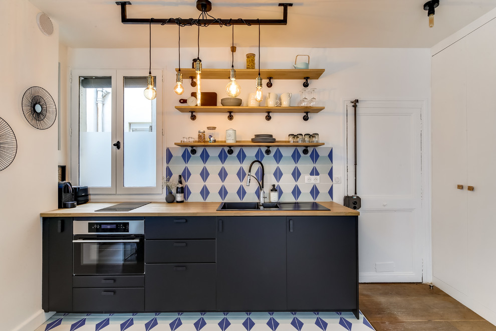 Photo of a small eclectic single-wall open plan kitchen in Paris with a double-bowl sink, black cabinets, wood benchtops, multi-coloured splashback, stone tile splashback, panelled appliances, ceramic floors and multi-coloured floor.
