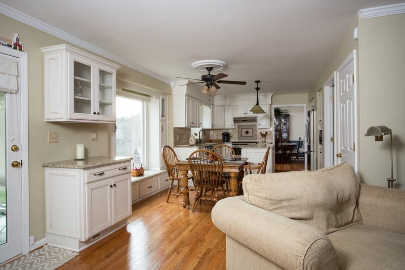 Inspiration for a mid-sized transitional open concept and l-shaped medium tone wood floor eat-in kitchen remodel with a bar, no fireplace, an island, shaker cabinets, white cabinets, granite countertops, beige backsplash, stone tile backsplash, stainless steel appliances and a double-bowl sink