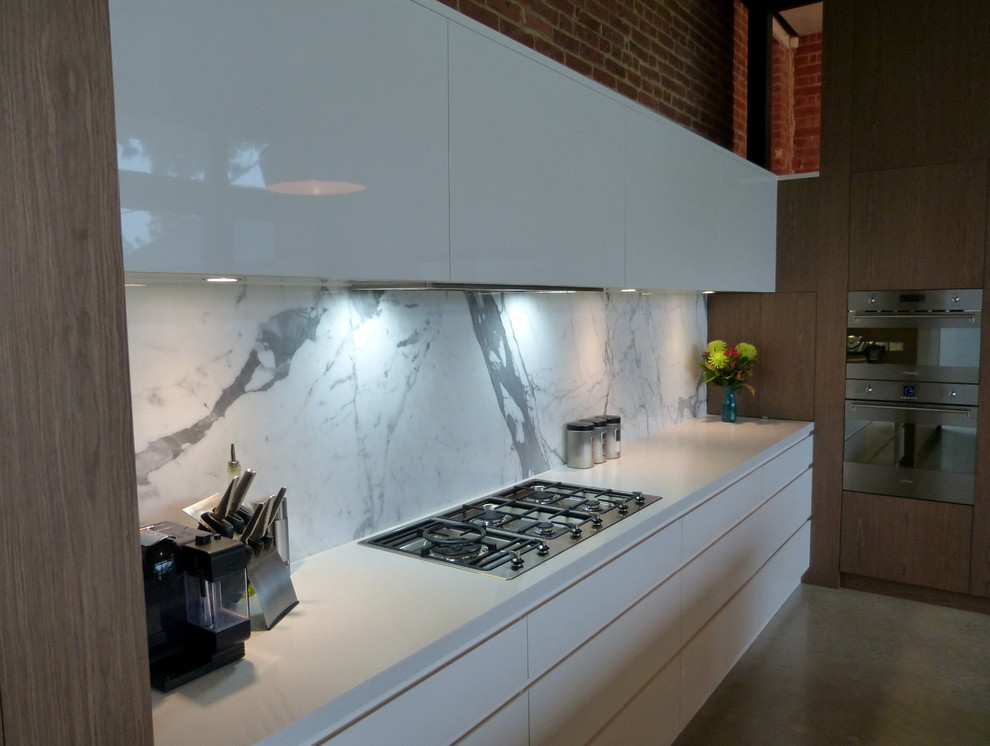 Photo of an expansive industrial l-shaped open plan kitchen in Adelaide with an undermount sink, flat-panel cabinets, white cabinets, quartz benchtops, multi-coloured splashback, marble splashback, stainless steel appliances, concrete floors, with island and grey floor.