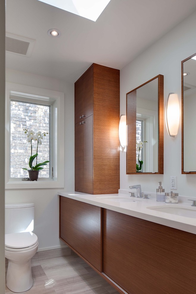 This is an example of a small modern 3/4 bathroom in Toronto with an undermount sink, flat-panel cabinets, medium wood cabinets, engineered quartz benchtops, an alcove tub, an alcove shower, a two-piece toilet, gray tile, stone tile, white walls and travertine floors.