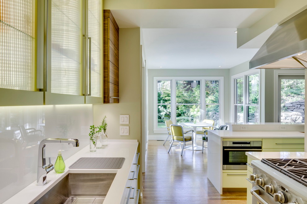 Inspiration for a large modern open plan kitchen in New York with an undermount sink, flat-panel cabinets, white splashback, glass sheet splashback, yellow cabinets, stainless steel appliances, light hardwood floors and with island.