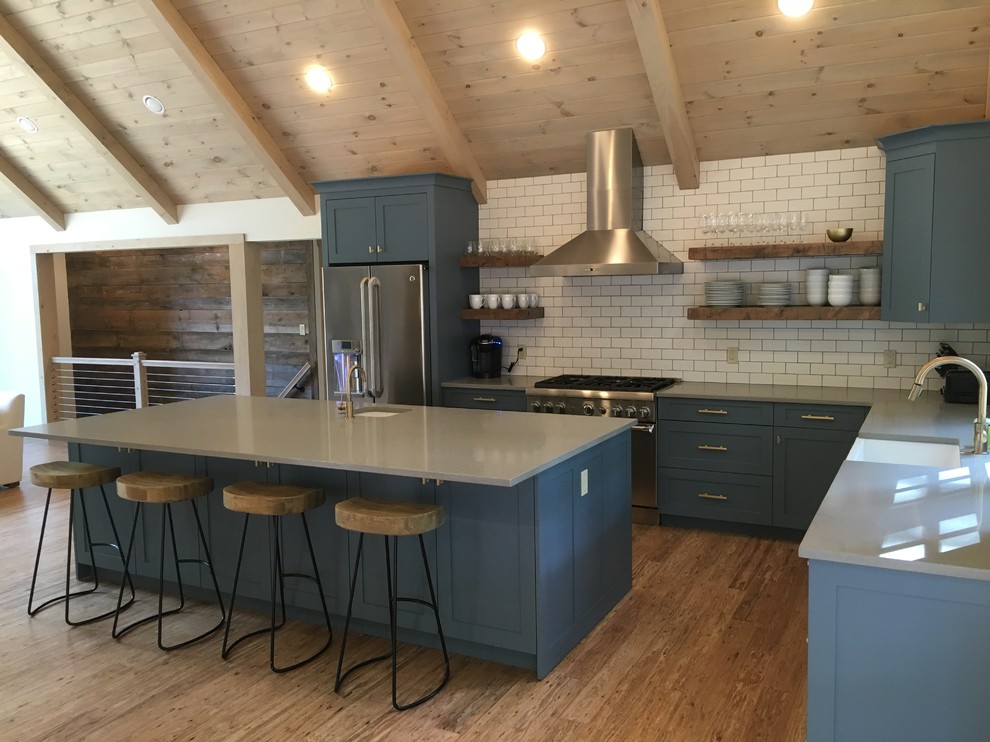 Photo of a mid-sized transitional l-shaped open plan kitchen in Boston with a farmhouse sink, shaker cabinets, blue cabinets, quartz benchtops, white splashback, subway tile splashback, stainless steel appliances, medium hardwood floors and with island.