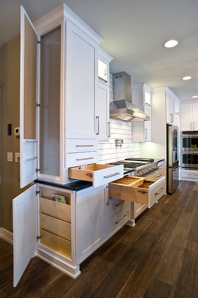 Inspiration for a large transitional l-shaped dark wood floor and brown floor eat-in kitchen remodel with an undermount sink, white cabinets, granite countertops, white backsplash, subway tile backsplash, stainless steel appliances, an island and shaker cabinets