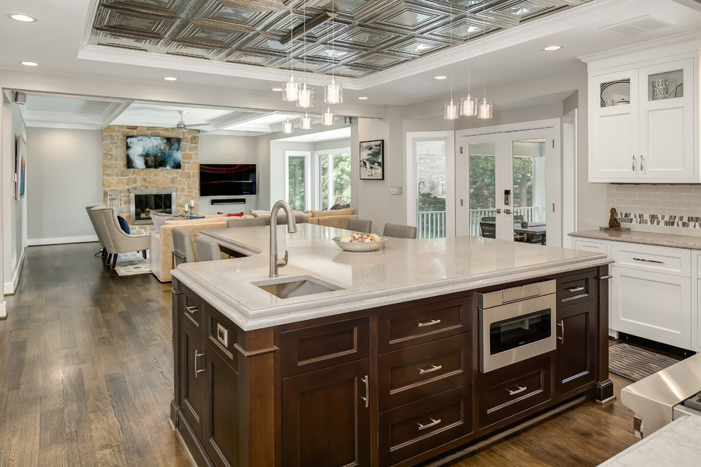 Example of a mid-sized transitional u-shaped dark wood floor and brown floor eat-in kitchen design in DC Metro with an undermount sink, shaker cabinets, white cabinets, solid surface countertops, beige backsplash, porcelain backsplash, stainless steel appliances and an island