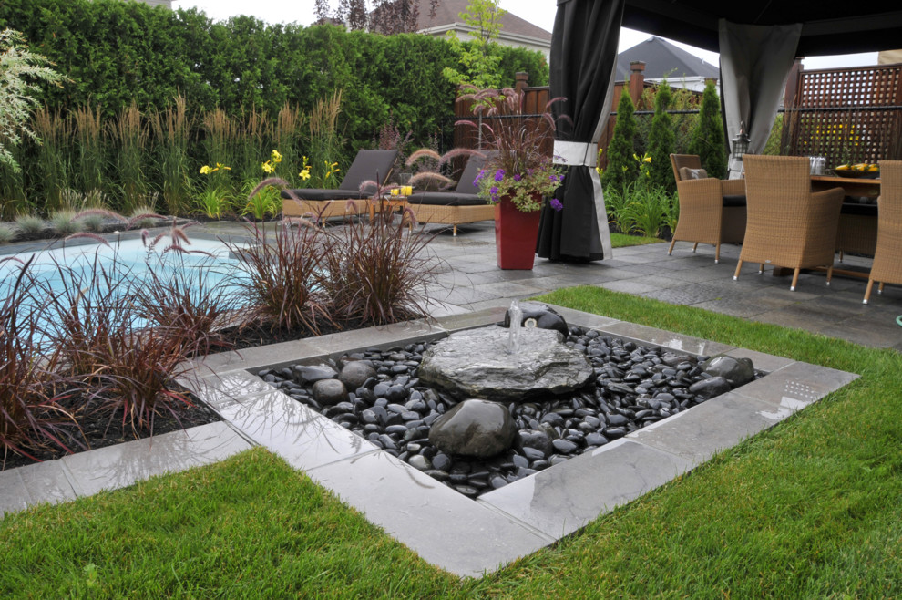 Photo of a contemporary backyard full sun garden in Montreal with a water feature and natural stone pavers.