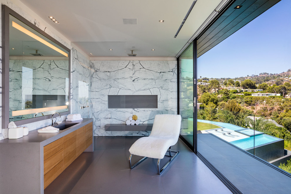 This is an example of a large contemporary master bathroom in Los Angeles with flat-panel cabinets, medium wood cabinets, an open shower, white tile, an integrated sink, an open shower, marble, grey walls, concrete floors, concrete benchtops, grey floor and grey benchtops.