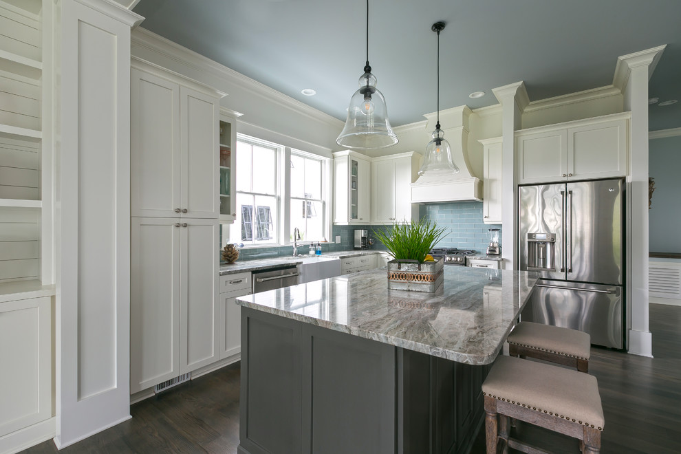 Inspiration for a large beach style l-shaped kitchen in Charleston with a farmhouse sink, shaker cabinets, white cabinets, green splashback, glass tile splashback, stainless steel appliances, dark hardwood floors, with island and brown floor.