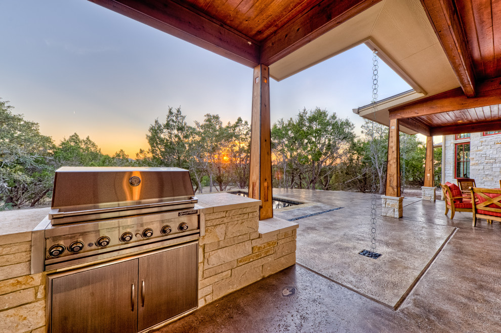 This is an example of a large traditional backyard patio in Austin with an outdoor kitchen, stamped concrete and a roof extension.