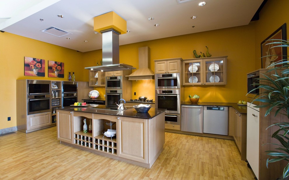 Large modern l-shaped eat-in kitchen in San Francisco with a single-bowl sink, glass-front cabinets, medium wood cabinets, onyx benchtops, yellow splashback, cement tile splashback, stainless steel appliances, light hardwood floors, with island, brown floor and black benchtop.