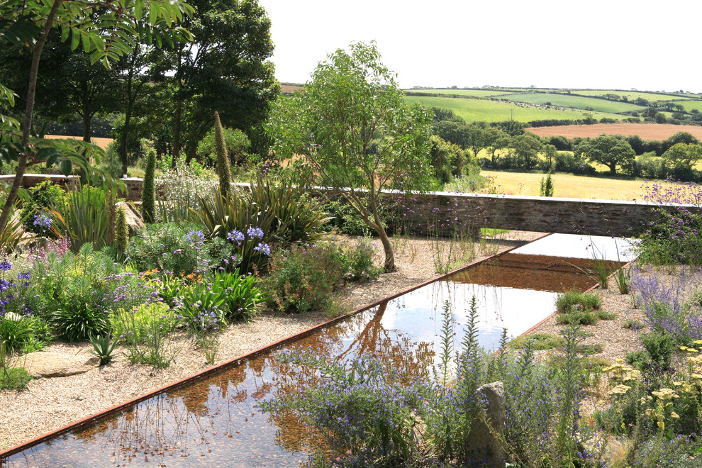 Photo of an expansive country sloped partial sun garden in Cornwall with a water feature and gravel.