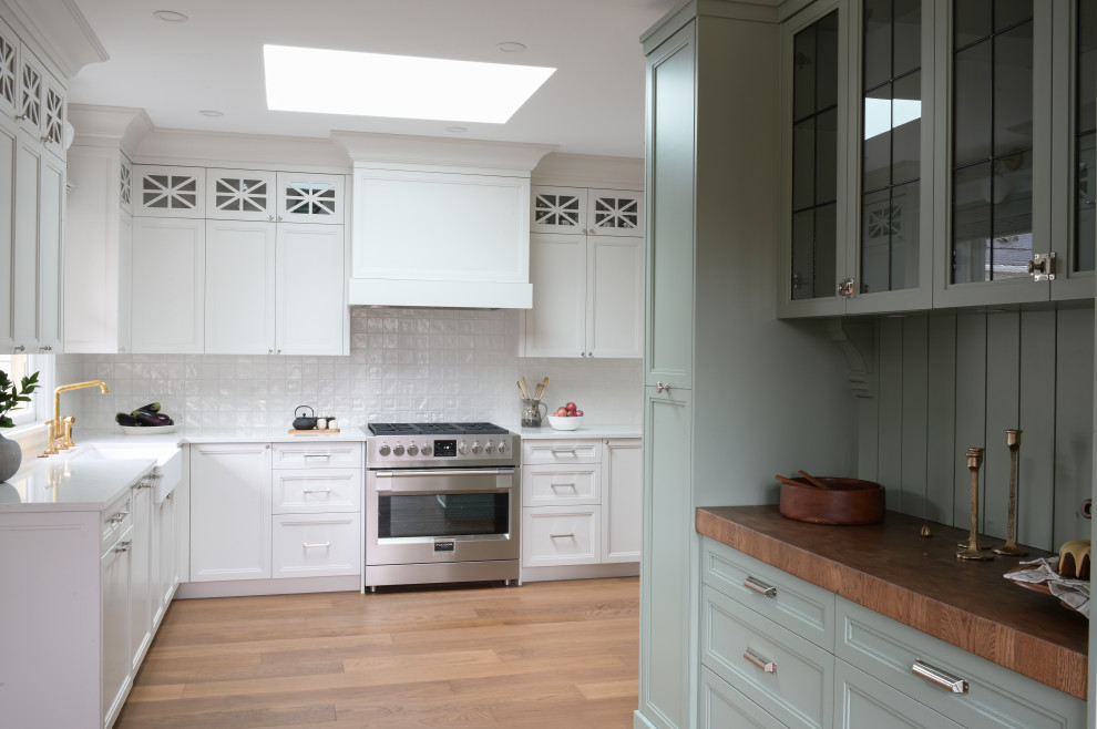Design ideas for a medium sized traditional l-shaped kitchen/diner in Vancouver with a belfast sink, shaker cabinets, white cabinets, engineered stone countertops, white splashback, ceramic splashback, stainless steel appliances, medium hardwood flooring, no island and white worktops.