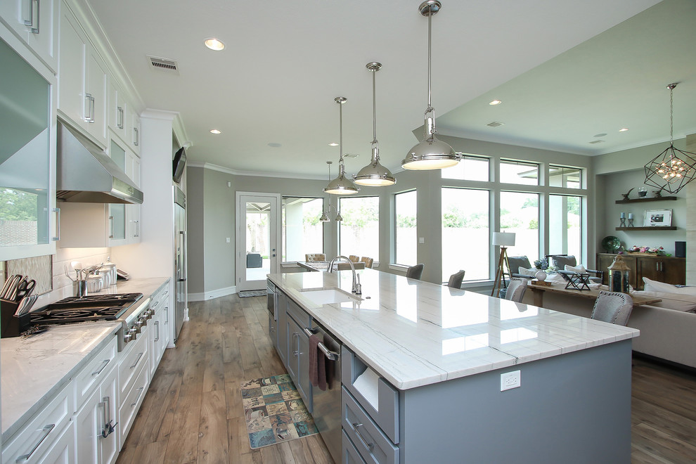 Transitional l-shaped open plan kitchen in Houston with an undermount sink, shaker cabinets, white cabinets, quartzite benchtops, white splashback, subway tile splashback, stainless steel appliances, ceramic floors, with island and grey benchtop.