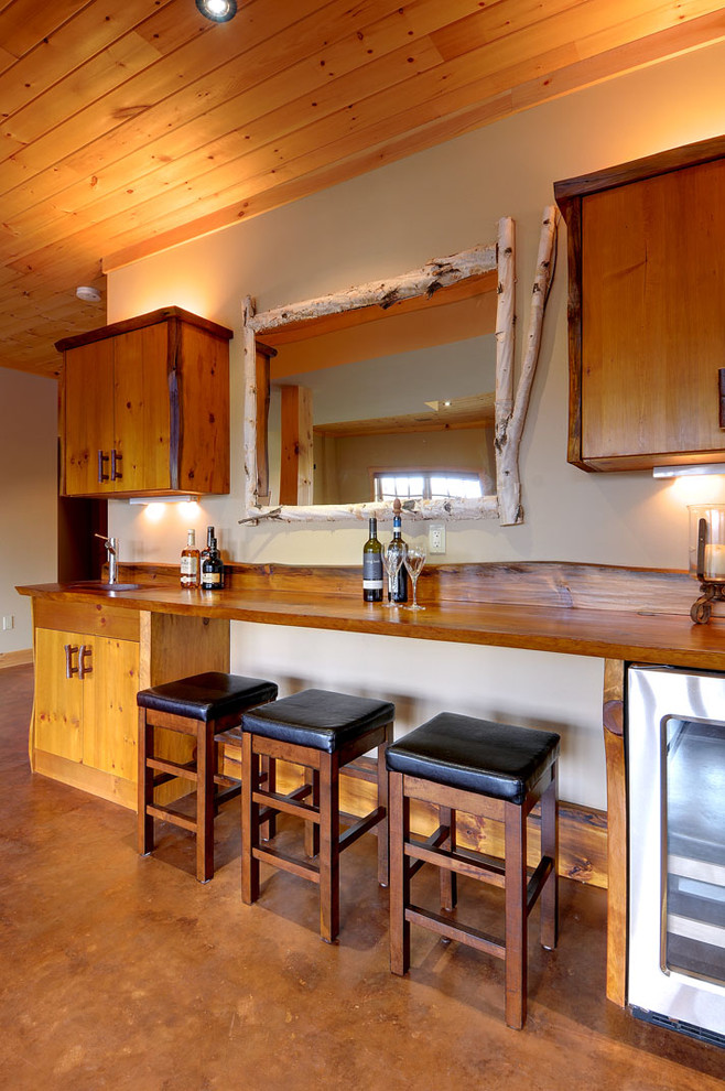 Photo of a mid-sized country single-wall seated home bar in Toronto with concrete floors, flat-panel cabinets, medium wood cabinets, wood benchtops and brown benchtop.