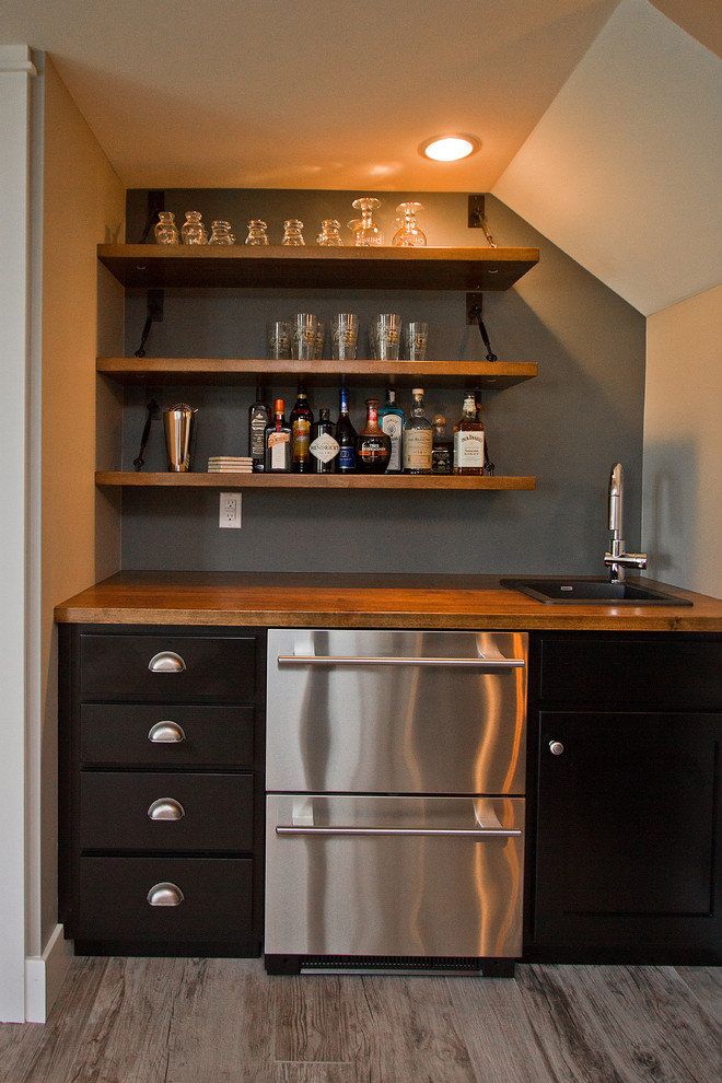 Inspiration for a large arts and crafts single-wall wet bar in Other with carpet, beige floor, a drop-in sink, black cabinets, wood benchtops, grey splashback, brown benchtop and flat-panel cabinets.