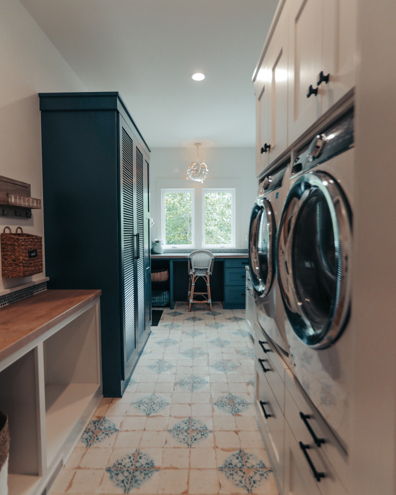 Design ideas for an expansive beach style utility room in Other with blue cabinets, wood benchtops, blue splashback, glass tile splashback, white walls, ceramic floors, a stacked washer and dryer, multi-coloured floor and brown benchtop.