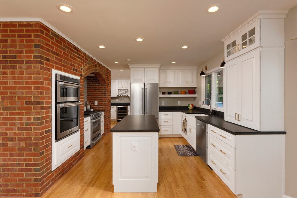 Mid-sized transitional galley light wood floor enclosed kitchen photo in DC Metro with a farmhouse sink, raised-panel cabinets, white cabinets, solid surface countertops, stainless steel appliances, an island and gray backsplash