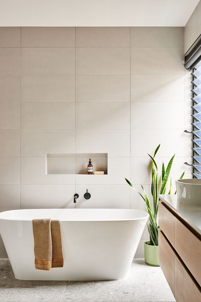 Foto på ett stort funkis vit en-suite badrum, med skåp i ljust trä, ett fristående badkar, grå kakel, porslinskakel, grå väggar, klinkergolv i porslin, bänkskiva i kvartsit och grått golv