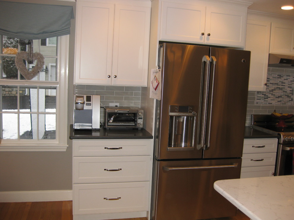 Inspiration for a transitional l-shaped medium tone wood floor eat-in kitchen remodel in Boston with white cabinets, an island, an undermount sink, quartz countertops, stainless steel appliances, shaker cabinets, green backsplash, subway tile backsplash and black countertops