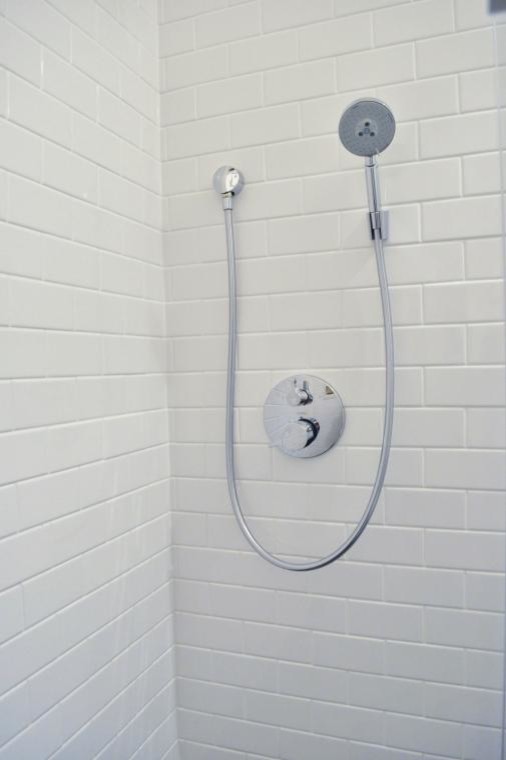 Photo of a small modern 3/4 bathroom in New York with a wall-mount sink, flat-panel cabinets, white cabinets, glass benchtops, a corner shower, white tile, subway tile, white walls, a two-piece toilet and vinyl floors.