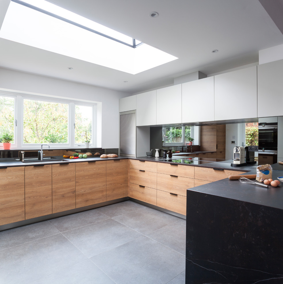 Design ideas for an expansive modern u-shaped open plan kitchen in London with flat-panel cabinets, mirror splashback, grey floors, an integrated sink, light wood cabinets, composite countertops, stainless steel appliances, no island and metallic splashback.