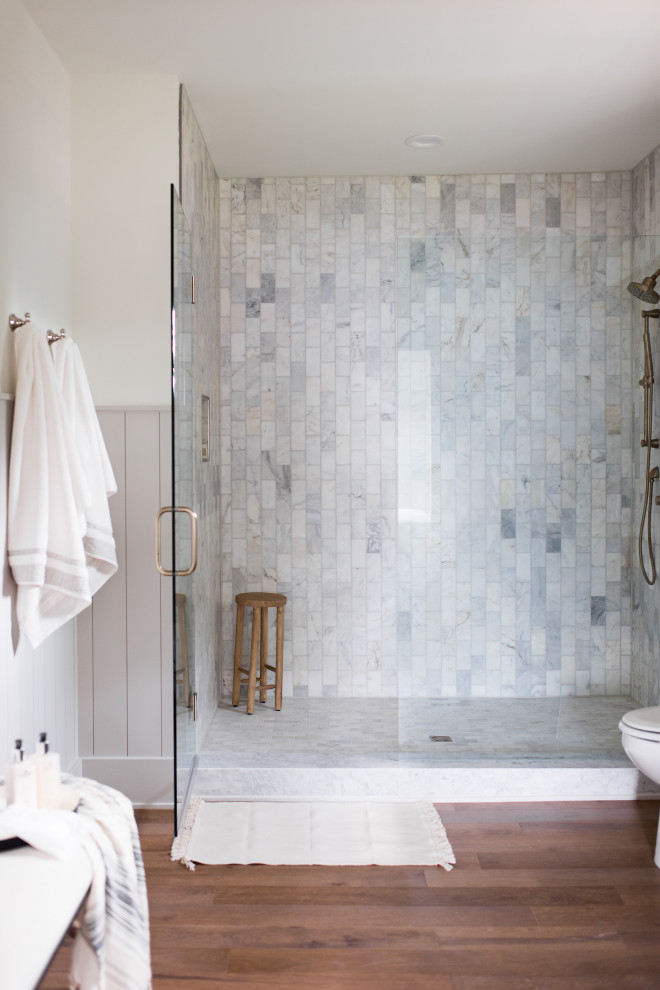 Inspiration for a mid-sized transitional master bathroom in Indianapolis with shaker cabinets, black cabinets, marble, medium hardwood floors, an undermount sink, marble benchtops, brown floor, a hinged shower door, a niche, a double vanity and planked wall panelling.