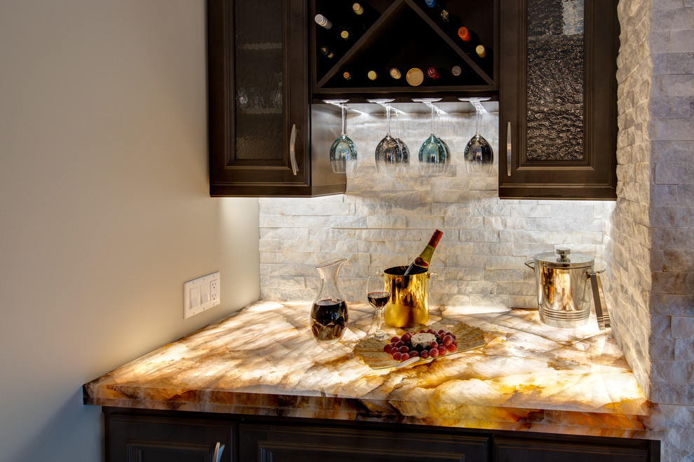Small transitional single-wall home bar in Edmonton with no sink, glass-front cabinets, brown cabinets, white splashback, stone tile splashback, multi-coloured benchtop and onyx benchtops.