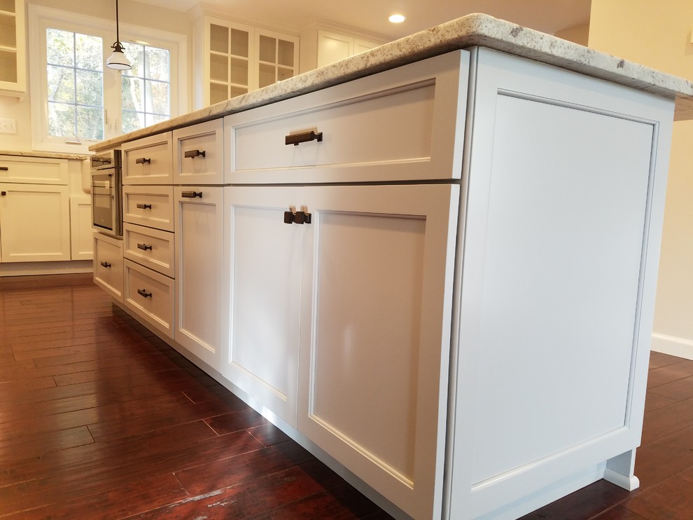 Example of a mid-sized transitional l-shaped dark wood floor and brown floor eat-in kitchen design with a farmhouse sink, shaker cabinets, white cabinets, granite countertops, white backsplash, subway tile backsplash, stainless steel appliances and an island