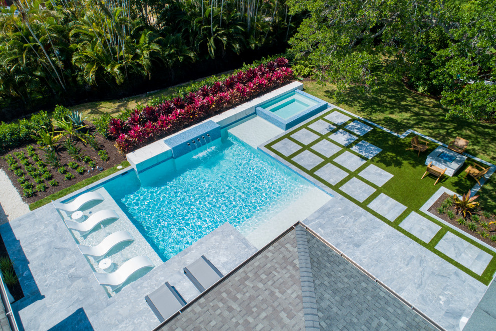 Photo of a large modern backyard custom-shaped pool in Miami with a water feature and natural stone pavers.
