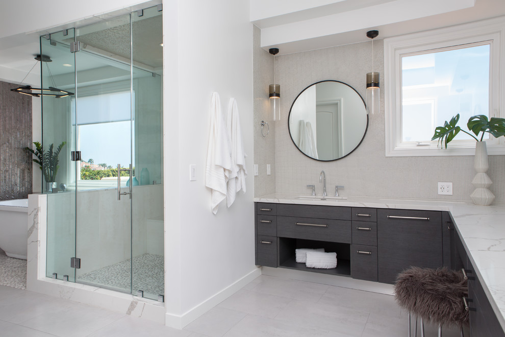 Inspiration for a contemporary bathroom in Los Angeles with flat-panel cabinets, grey cabinets, a freestanding tub, a corner shower, white walls, an undermount sink, grey floor, a hinged shower door and white benchtops.