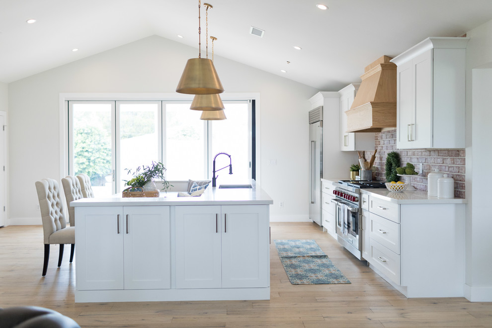 Inspiration for a large transitional galley medium tone wood floor and brown floor eat-in kitchen remodel in Phoenix with an undermount sink, shaker cabinets, quartz countertops, brick backsplash, stainless steel appliances, white countertops, white cabinets, brown backsplash and an island