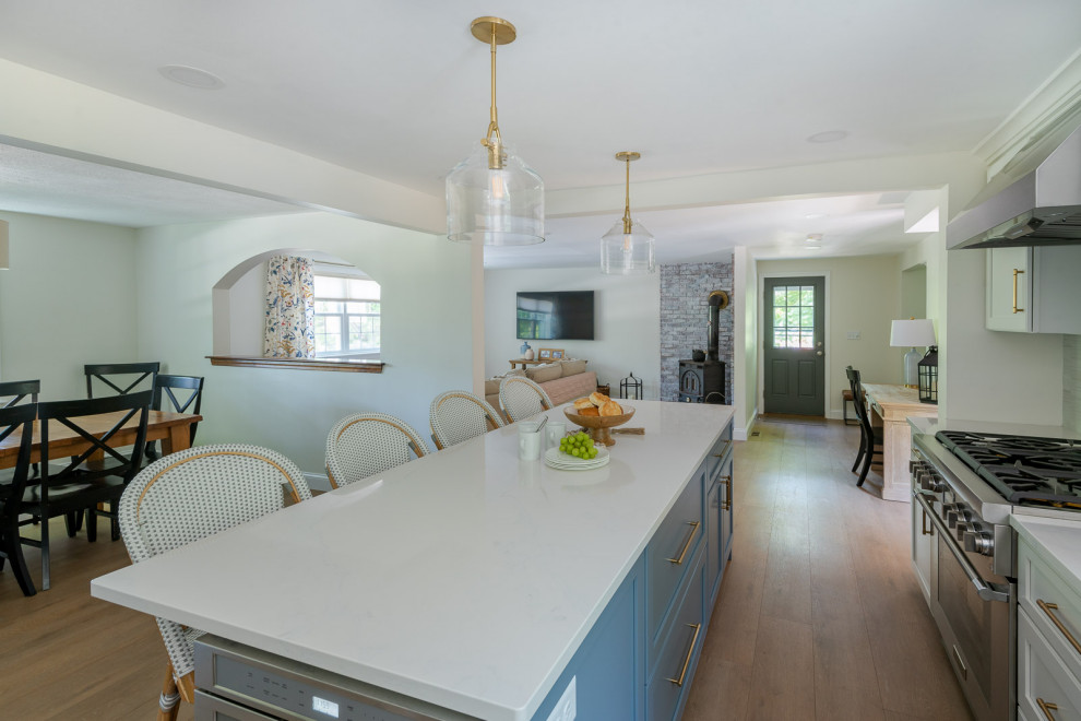 Example of a mid-sized transitional l-shaped light wood floor and brown floor eat-in kitchen design in Boston with an undermount sink, shaker cabinets, white cabinets, quartz countertops, gray backsplash, ceramic backsplash, stainless steel appliances, an island and white countertops