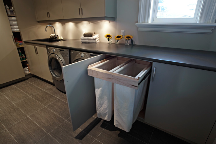 Mid-sized transitional u-shaped dedicated laundry room in Toronto with a drop-in sink, flat-panel cabinets, grey cabinets, laminate benchtops, white walls, ceramic floors, a side-by-side washer and dryer, grey floor and brown benchtop.