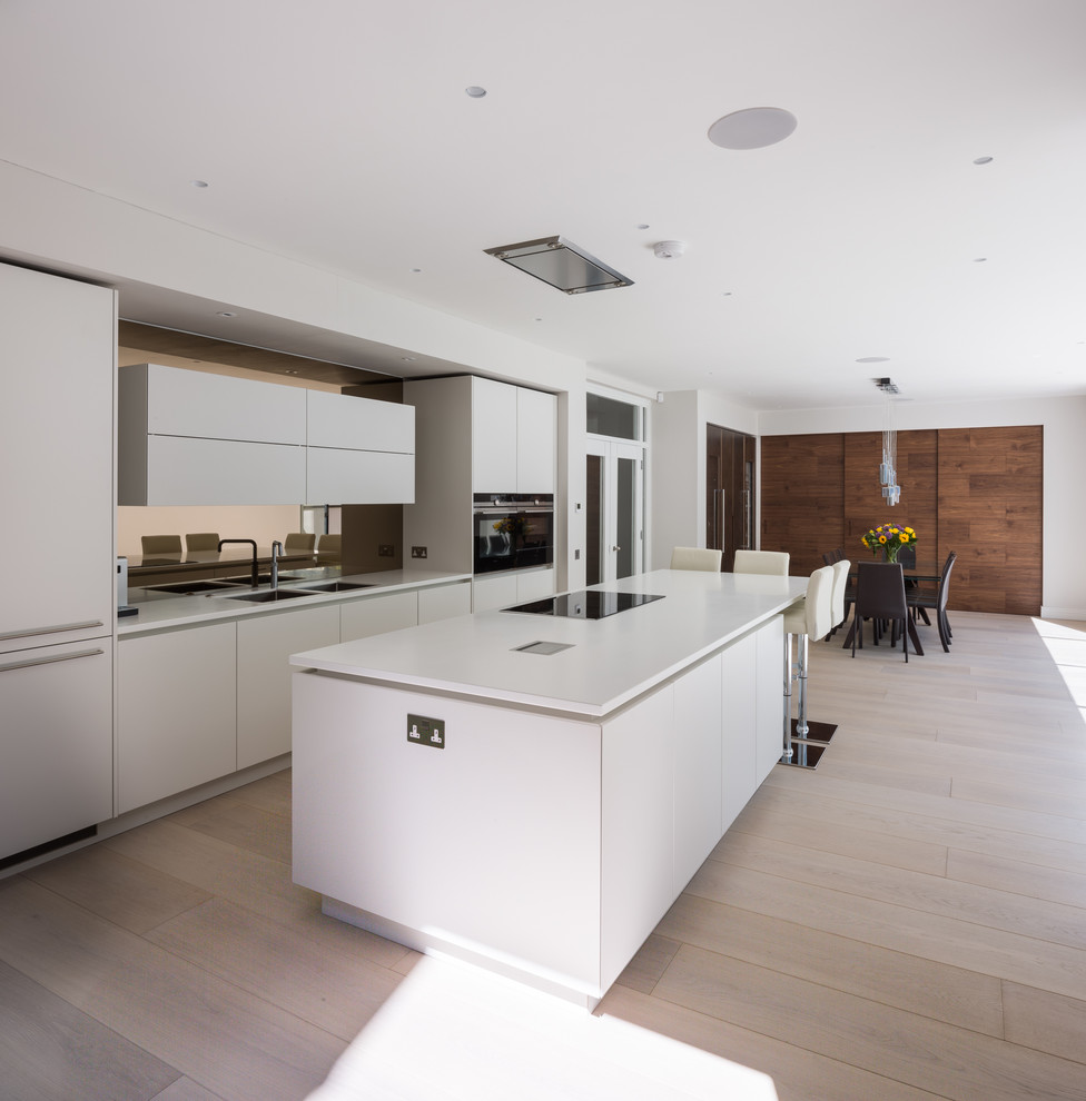 Inspiration for a large single-wall eat-in kitchen in London with an integrated sink, flat-panel cabinets, white cabinets, limestone benchtops, metallic splashback, light hardwood floors, with island, brown floor and white benchtop.