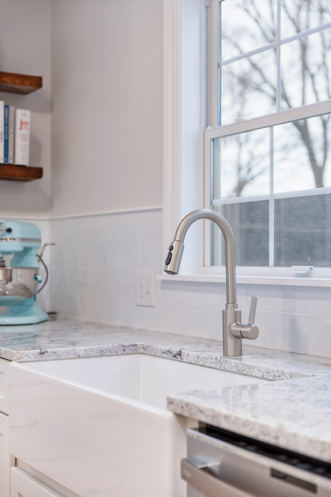 Example of a mid-sized transitional u-shaped medium tone wood floor eat-in kitchen design in Boston with a farmhouse sink, shaker cabinets, white cabinets, granite countertops, white backsplash, subway tile backsplash, stainless steel appliances, a peninsula and multicolored countertops
