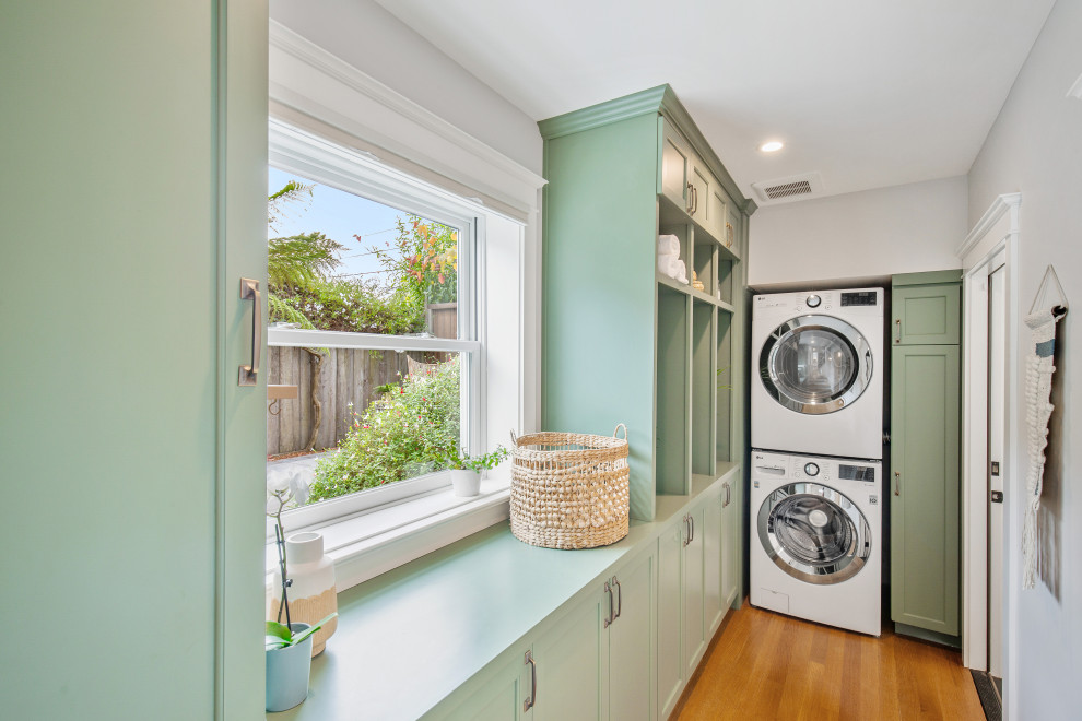 Foto di una sala lavanderia chic con ante in stile shaker, ante verdi, pareti bianche, lavatrice e asciugatrice a colonna, top verde e parquet chiaro