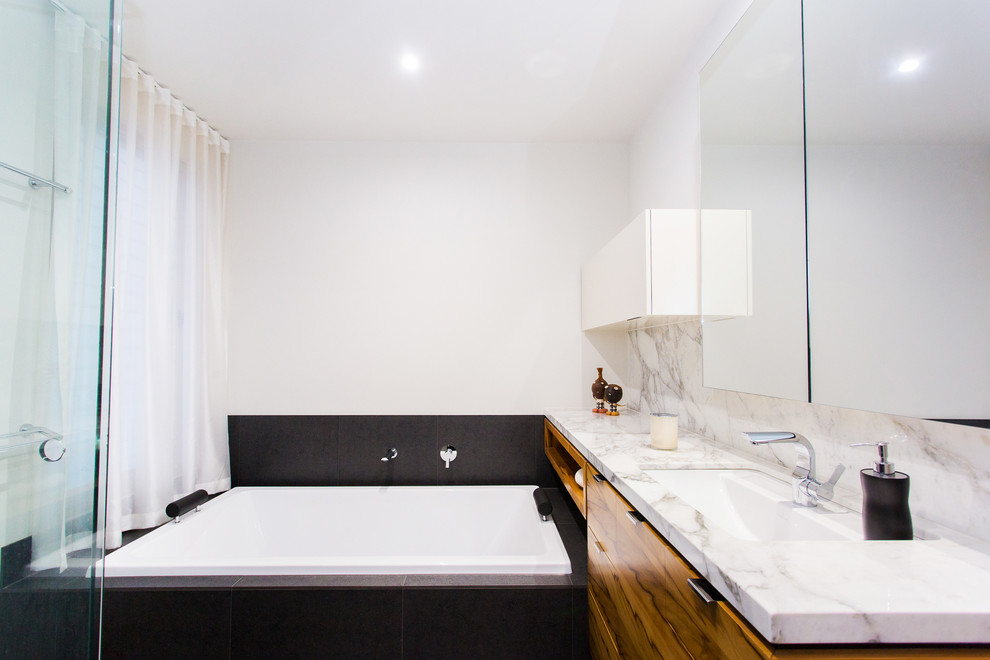 Inspiration for a mid-sized contemporary bathroom in Geelong with a drop-in sink, flat-panel cabinets, medium wood cabinets, marble benchtops, a drop-in tub, an open shower, a wall-mount toilet, gray tile, porcelain tile, grey walls and ceramic floors.