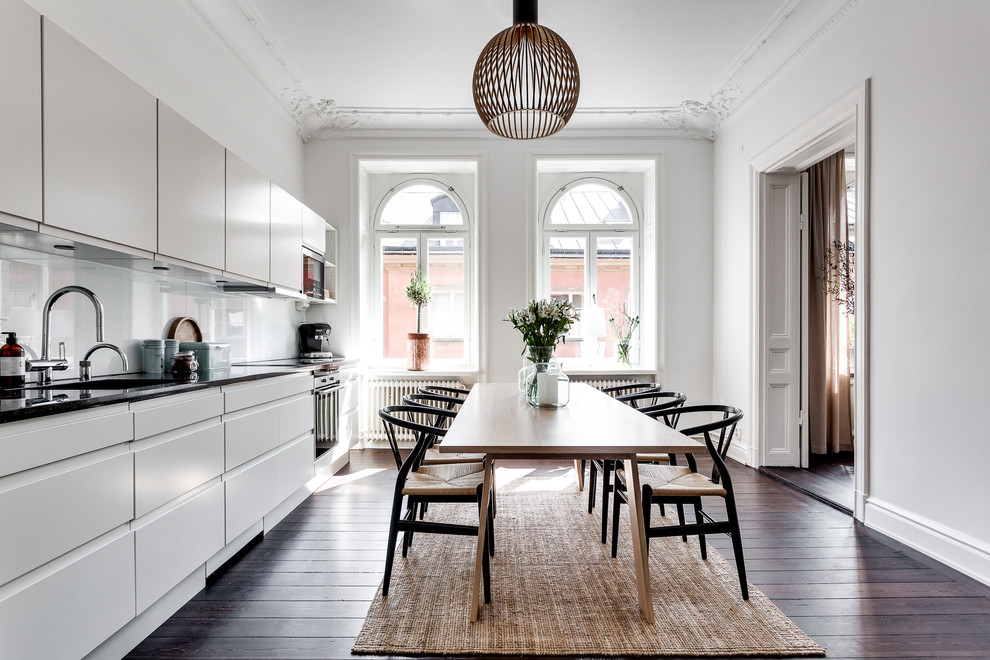 Photo of a mid-sized scandinavian single-wall eat-in kitchen in Stockholm with a single-bowl sink, flat-panel cabinets, white cabinets, stainless steel appliances, dark hardwood floors, no island, white splashback, glass sheet splashback and brown floor.