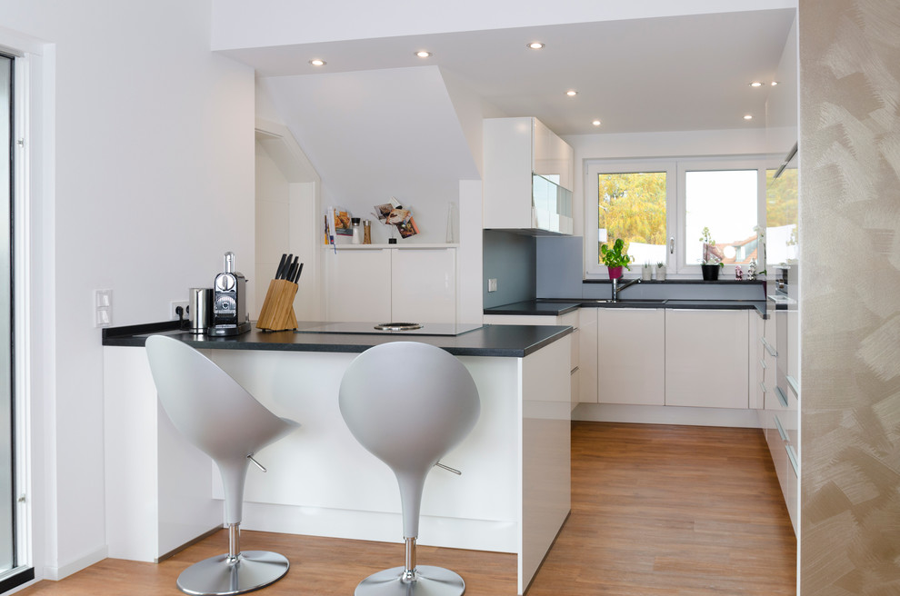 This is an example of a small contemporary open plan kitchen in Nuremberg with flat-panel cabinets, grey splashback, medium hardwood floors, a peninsula, a drop-in sink and white cabinets.